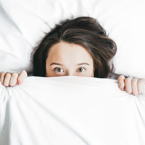 Woman in bed covering face with duvet. Emotional Reasons for Low Libido