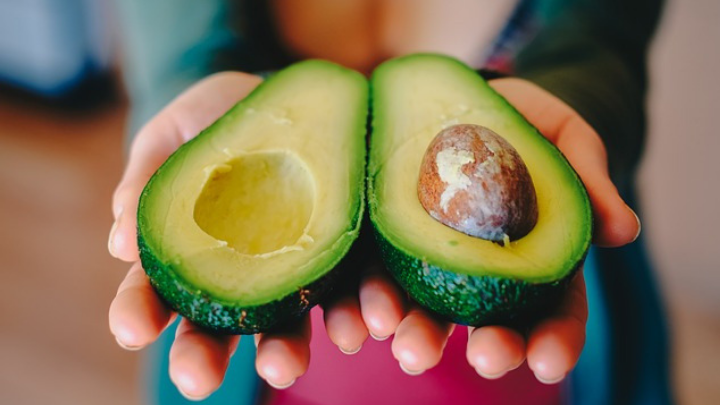 a lady holding an avocado which has been cut in half, representing good health as a featured image